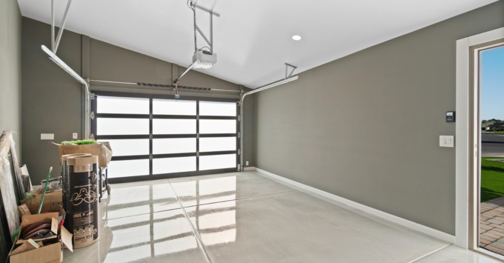 The interior of a garage with a glossy floor, gray walls, and storage boxes. The garage door is made of frosted glass panels.