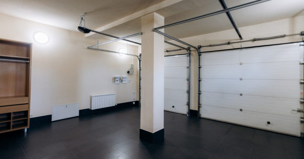 The interior of an empty three-car garage with cream-colored walls, a matte black floor, and white garage doors.