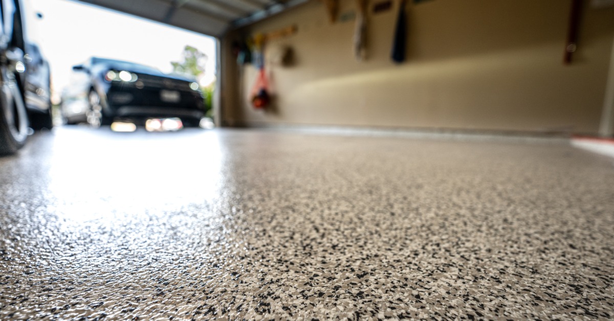 A ground-level view of a residential garage with a speckled epoxy floor. A black car is pulling into the garage.